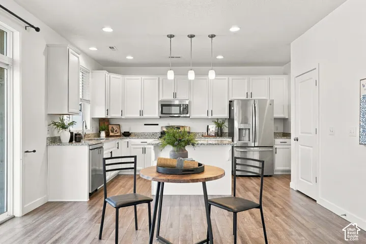Kitchen featuring white cabinetry with dark hardware, stainless steel appliances, speckled countertops, wood-finish flooring, and recessed lighting