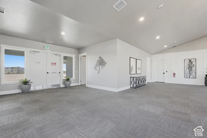 Recessed lighting, sloped ceiling, gray carpet tile flooring, white paneling, and multiple windows