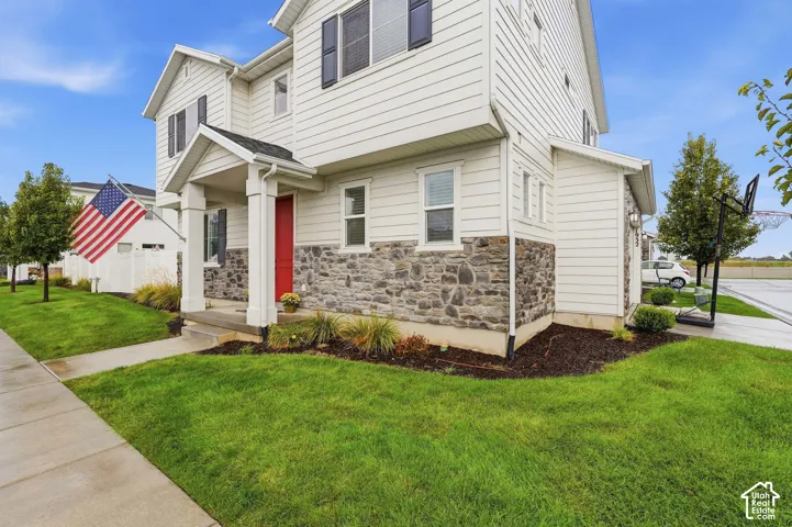White siding exterior with stone accents, covered front porch, vibrant red entry door, and a concrete pathway