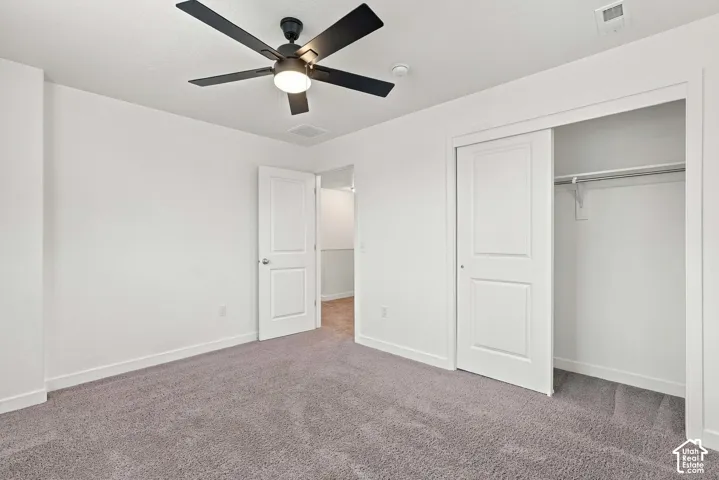 Spacious room featuring gray carpeting, white painted walls, a built-in closet with sliding doors, and a ceiling fan with integrated lighting