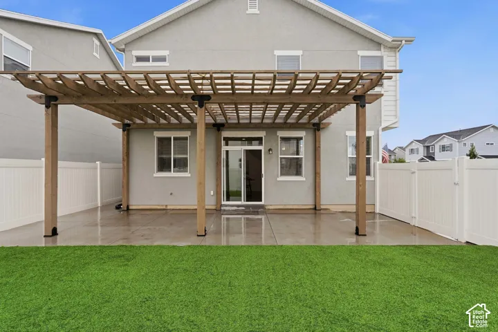 Expansive concrete patio with a wooden pergola, sliding glass door access, and a manicured lawn