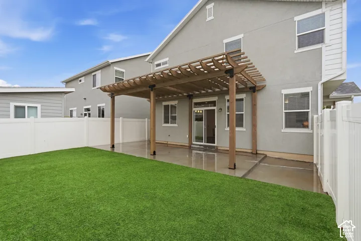 Pergola-covered concrete patio leading to a synthetic turf backyard