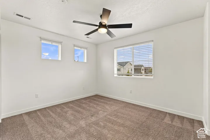 Warm neutral-toned carpeting, ceiling fan with integrated lighting, multiple windows with blinds, and white painted walls