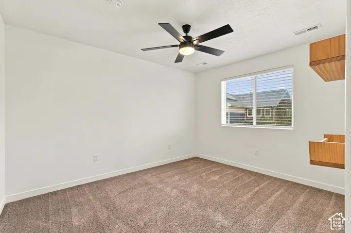 Neutral color palette, carpeted flooring, window with blinds, ceiling fan with integrated lighting, and built-in wood-finish shelving