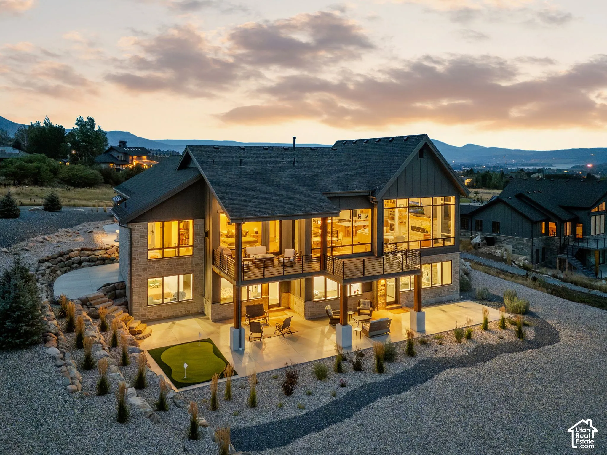 Stone and wood siding exterior with multiple balconies, expansive windows, a ground-level patio, and a putting green
