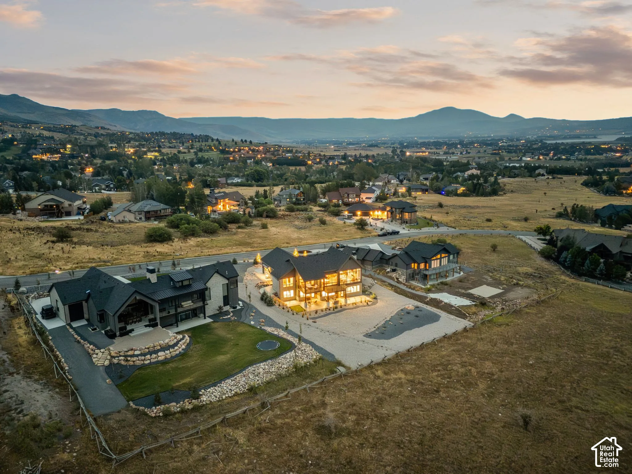 Mountain backdrop, illuminated residential structures, expansive open terrain, manicured lawn, stone retaining walls