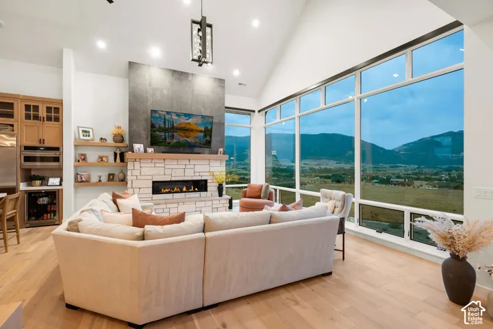 Vaulted ceilings with recessed lighting, floor-to-ceiling windows, stone-clad fireplace with wood mantle, wood-finish flooring, and built-in shelving
