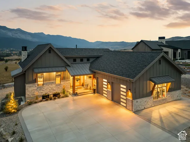Mountain backdrop, stone and board-and-batten exterior, prominent entry porch, two-car garage with modern doors, concrete driveway