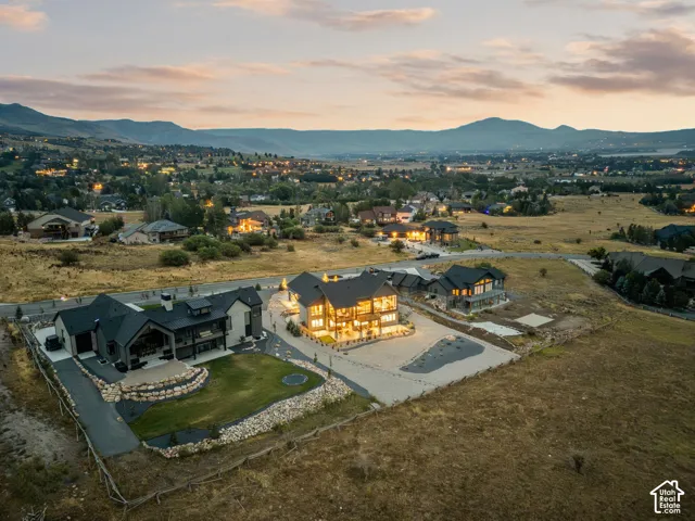 Mountain backdrop, illuminated residential structures, expansive open terrain, manicured lawn, stone retaining walls