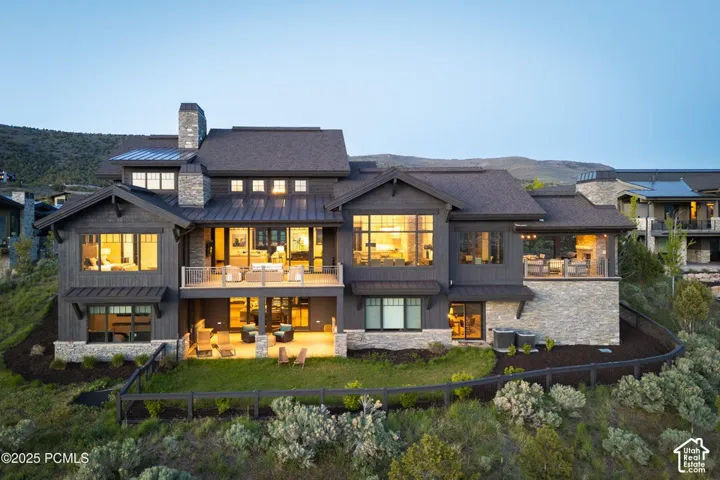 Multi-level exterior with extensive windows, stone and wood-finish siding, multiple balconies and patios, and an integrated stone chimney