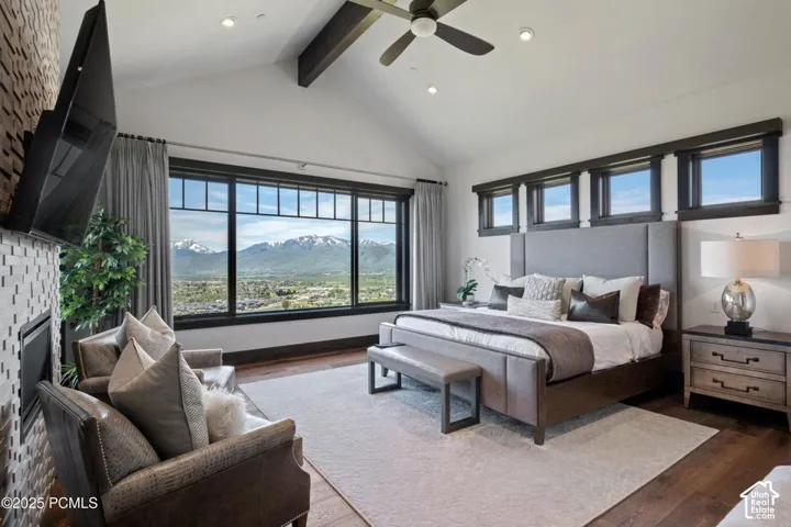Vaulted ceiling with exposed beam, expansive window framing mountain scenery, wood-finish flooring, fireplace with a tiled surround, and multiple transom windows