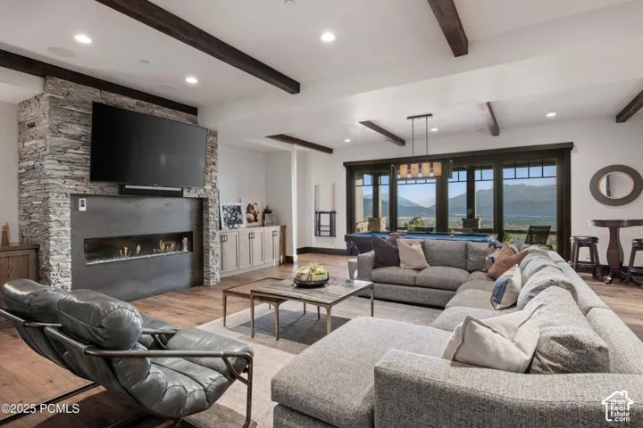 Stone-clad fireplace with a linear gas insert, wood-finish flooring, exposed ceiling beams, large windows, and built-in cabinetry