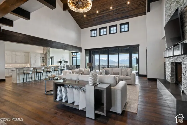Vaulted wood-paneled ceiling with exposed beams, wood-finish flooring, stone fireplace, and large sliding glass doors