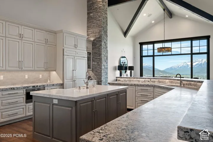 Kitchen featuring light-toned cabinetry, a spacious island with a contrasting base, stone countertops, a mosaic tile backsplash, and a prominent window