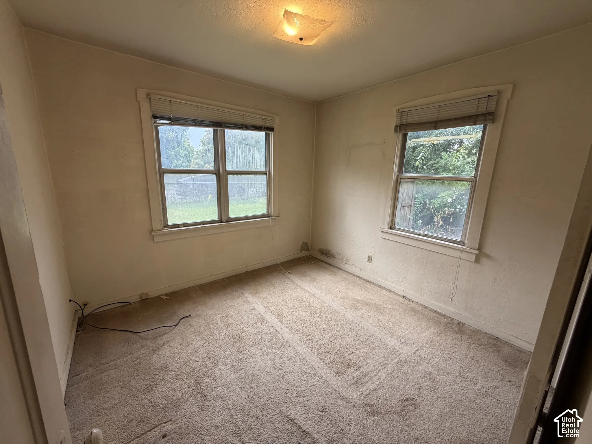 Recessed ceiling light fixture, two windows with horizontal blinds, and carpeted flooring