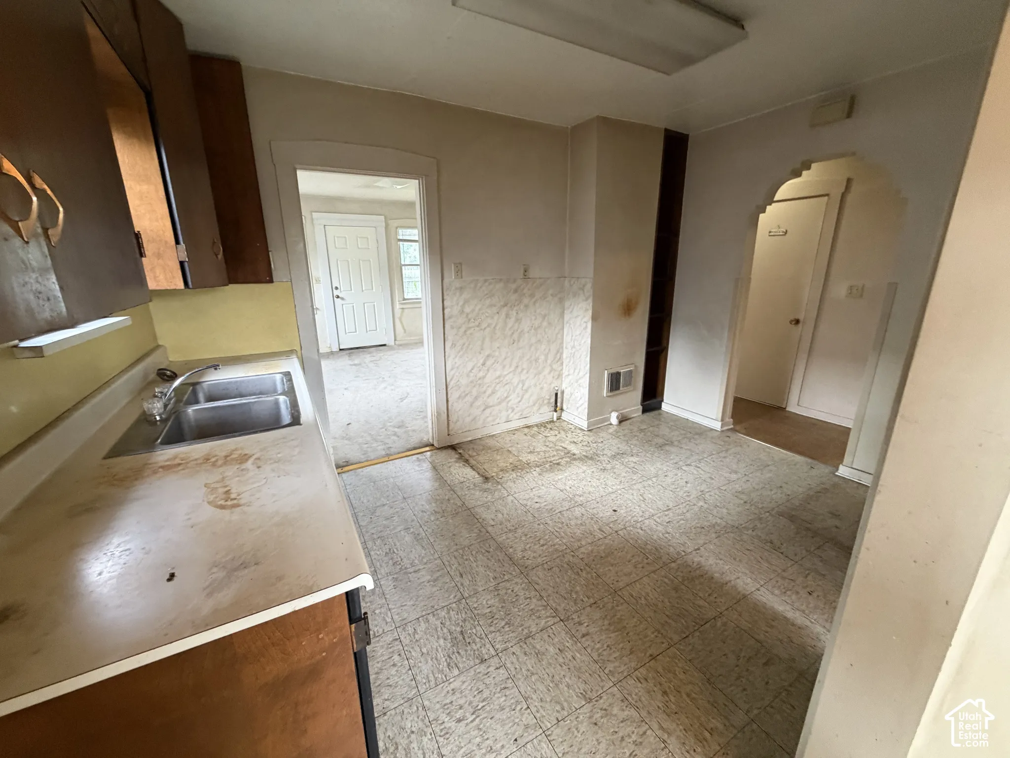 Kitchen featuring an integrated double-basin stainless steel sink, wood-finish cabinetry, and an arched doorway