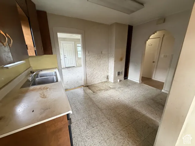 Kitchen featuring an integrated double-basin stainless steel sink, wood-finish cabinetry, and an arched doorway