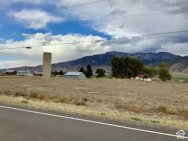 Expansive undeveloped land featuring natural ground cover, a paved road frontage, and distant mountain scenery