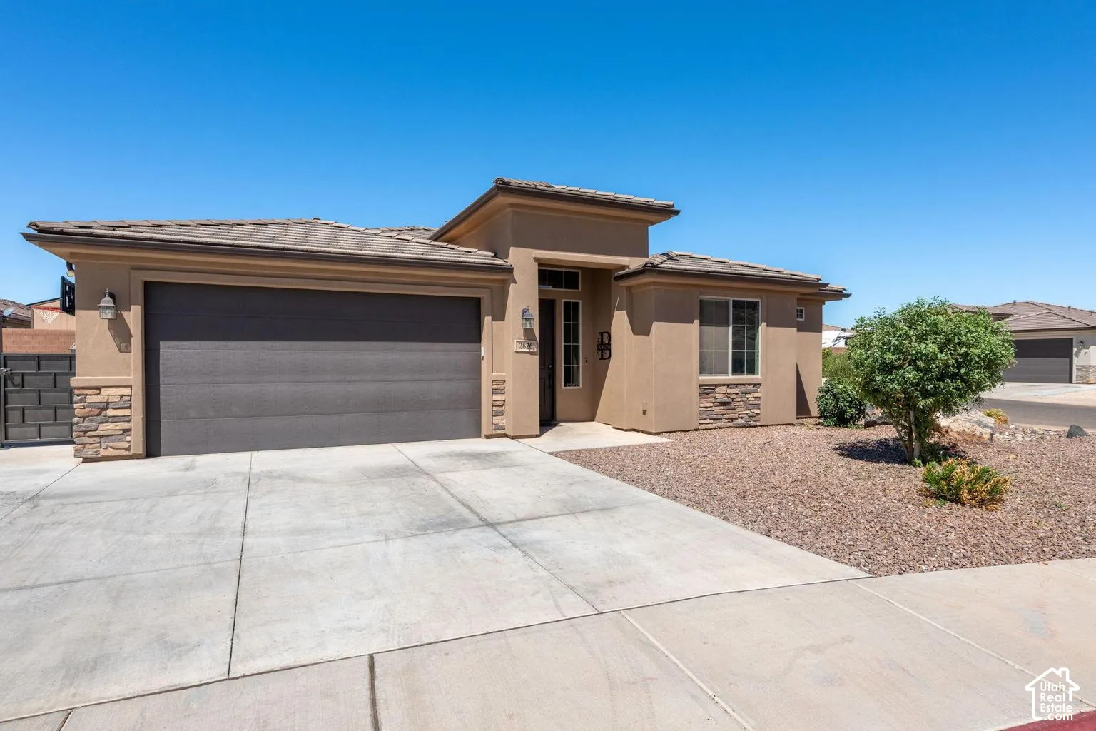 Stucco exterior with stone accents, concrete driveway, attached garage, tile roof, and desert landscaping