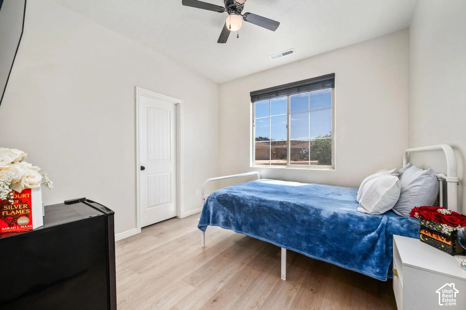 Light wood-finish flooring, a ceiling fan, a window with horizontal blinds, and a white paneled door