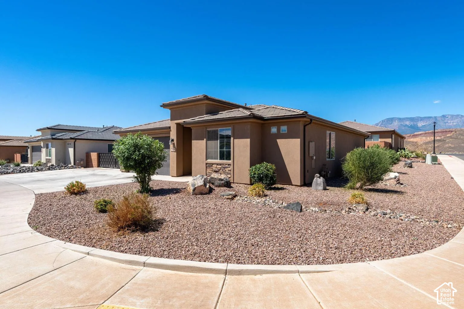 Desert landscaping with aggregate rock, stucco exterior, stone accenting, and a concrete driveway