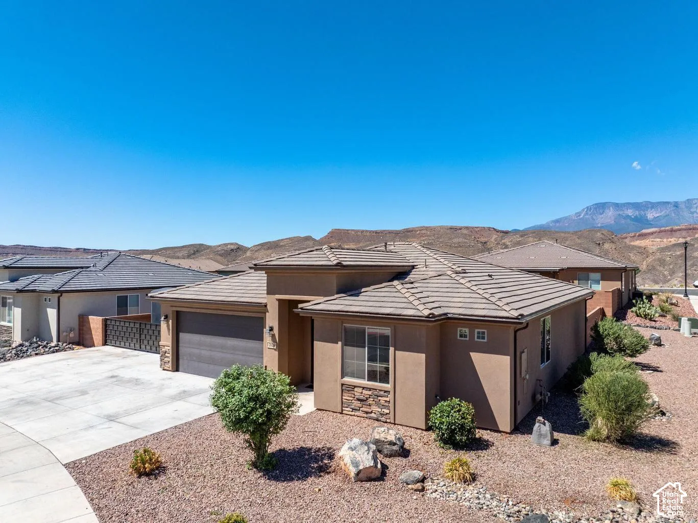 Exterior featuring a stucco finish, stone accents, a tile roof, an attached garage, and a concrete driveway