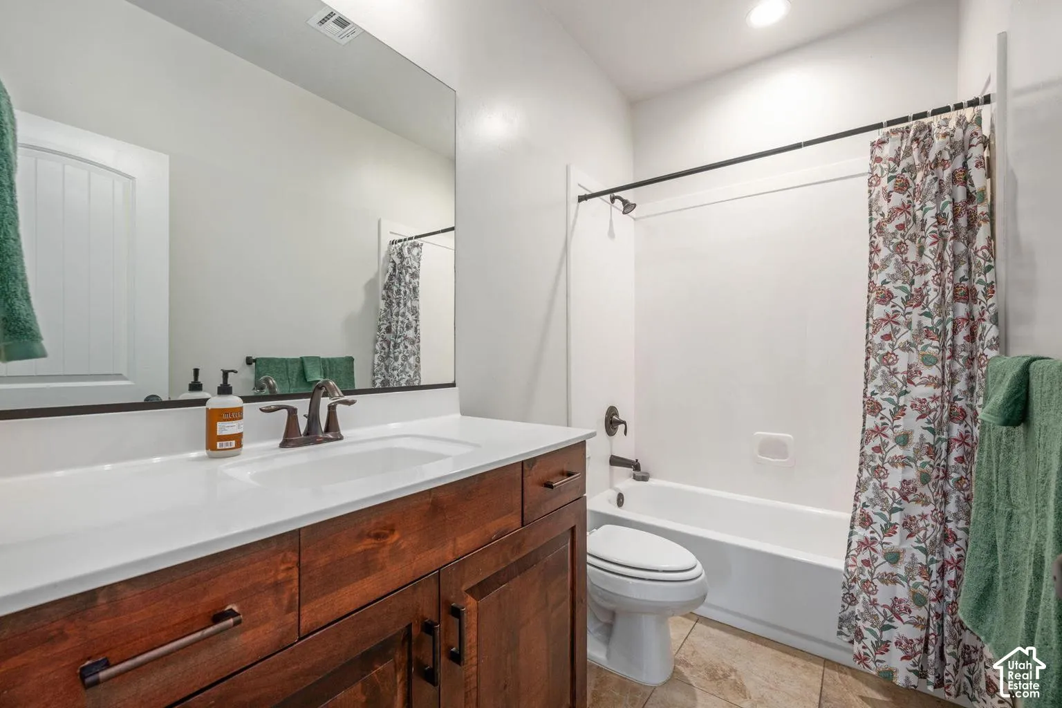Wood-finish vanity with a white countertop and undermount sink, bronze-finish fixtures, a large wall-mounted mirror, and tile flooring