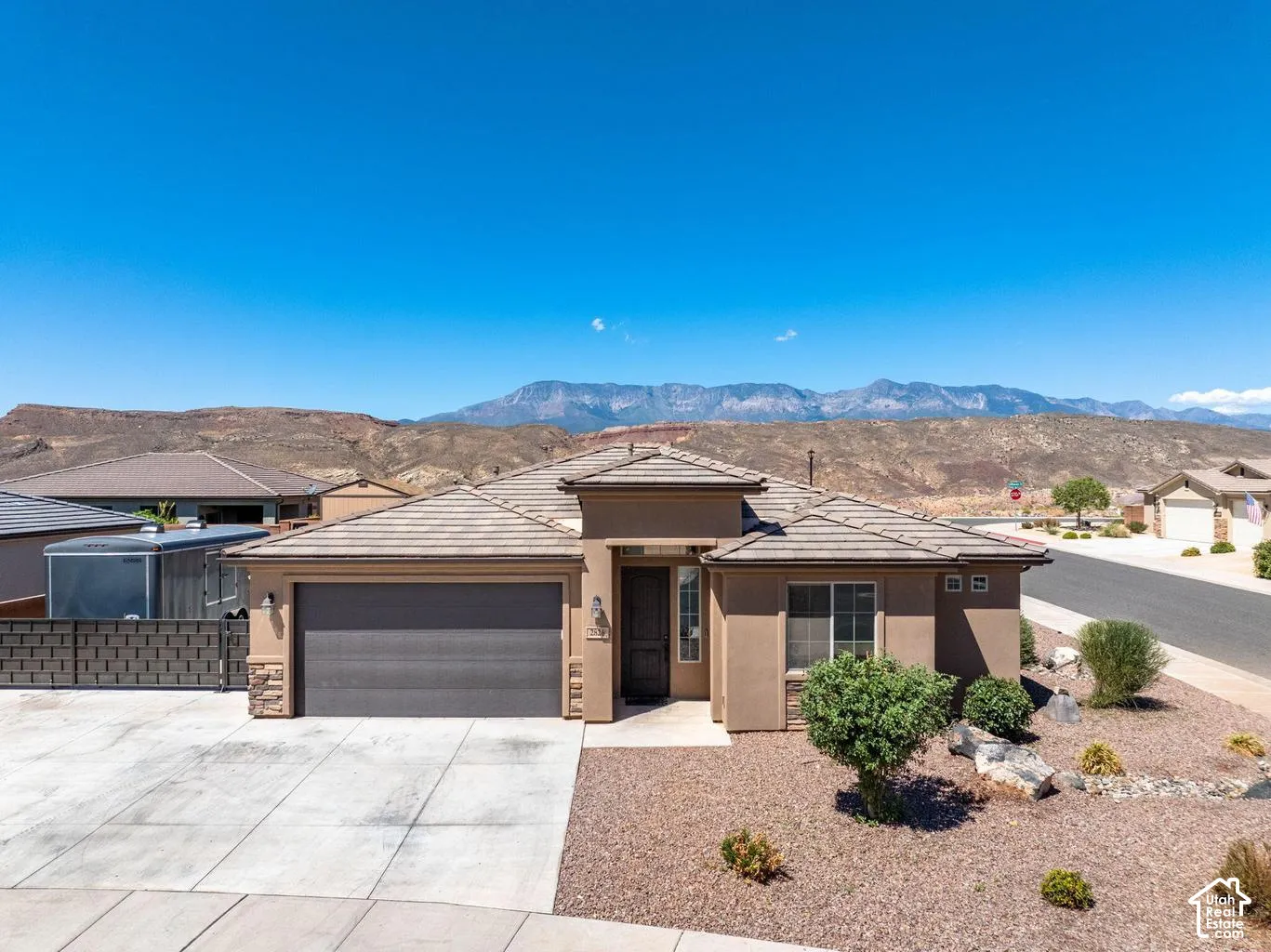 Stucco exterior with stone accents, a tile roof, an integrated garage, a concrete driveway, and desert landscaping