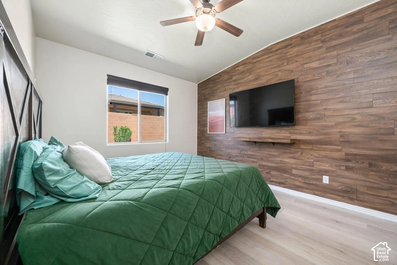 Accent wall with wood-finish paneling, light wood-finish flooring, and a ceiling fan with integrated lighting