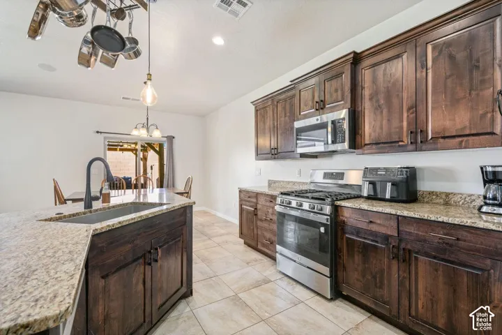 Kitchen featuring wood cabinetry, stainless steel appliances, granite countertops, an island with an undermount sink, and tiled flooring