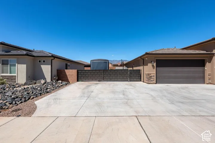 Concrete driveway with an integrated gate, stucco exterior with stone accents, and an attached garage