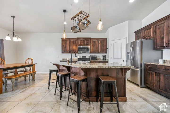 Kitchen featuring dark wood-finish cabinetry, stainless steel appliances, a large island with a stone countertop, and tile flooring