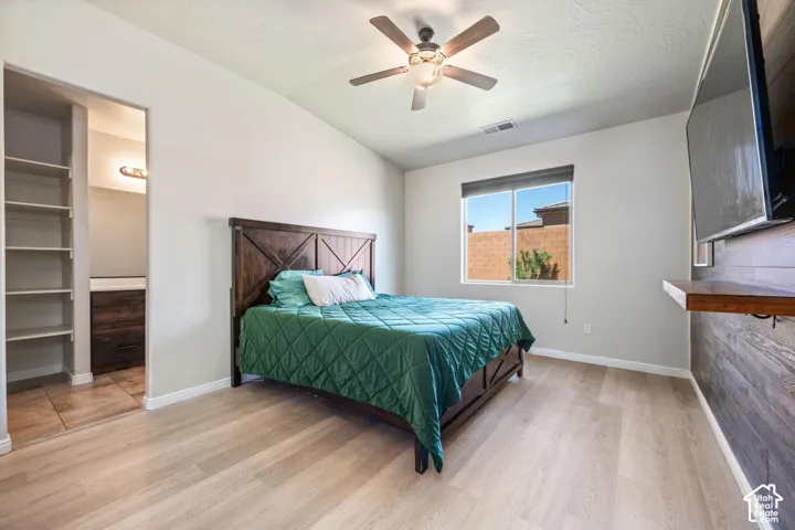 Vaulted ceiling, wood-finish flooring, ceiling fan with integrated lighting, built-in shelving, and wood-paneled accent wall with floating shelf