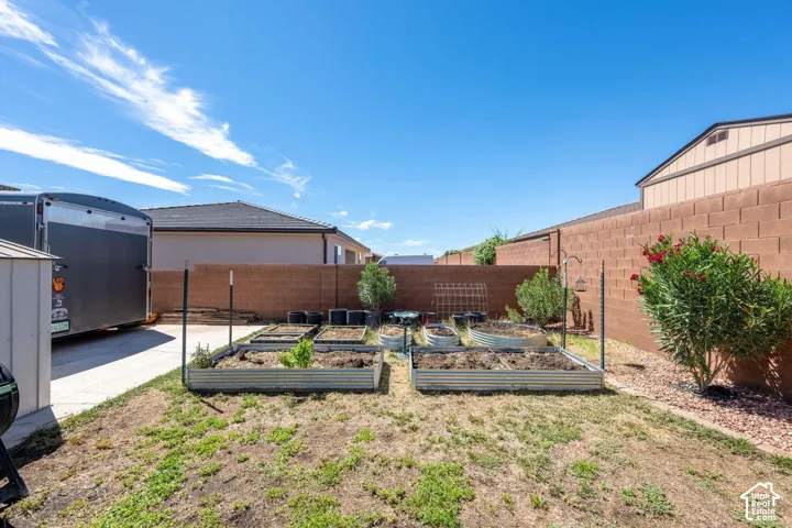 Backyard featuring multiple raised garden beds, a concrete block privacy wall, and a concrete driveway