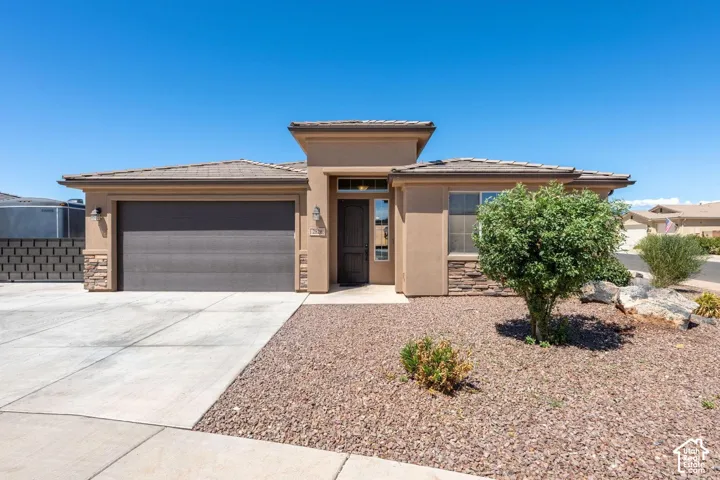 Stucco exterior with stone accents, covered entry, attached garage, and a gravel front yard with mature landscaping