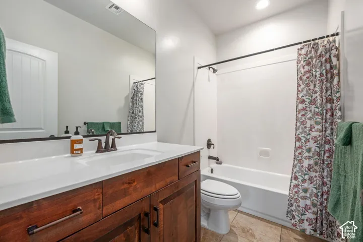 Wood-finish vanity with a white countertop and undermount sink, bronze-finish fixtures, a large wall-mounted mirror, and tile flooring