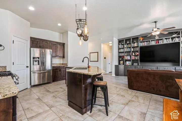 Kitchen island with a granite countertop, stainless steel appliances, dark wood cabinetry, tile flooring, and a built-in media center with shelving