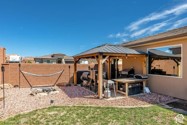 Backyard featuring a covered patio structure, a built-in fire pit area with gravel, and a partial lawn