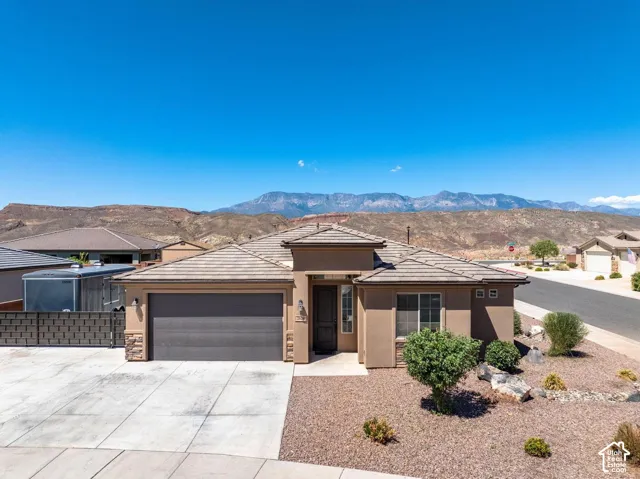Stucco exterior with stone accents, a tile roof, an integrated garage, a concrete driveway, and desert landscaping