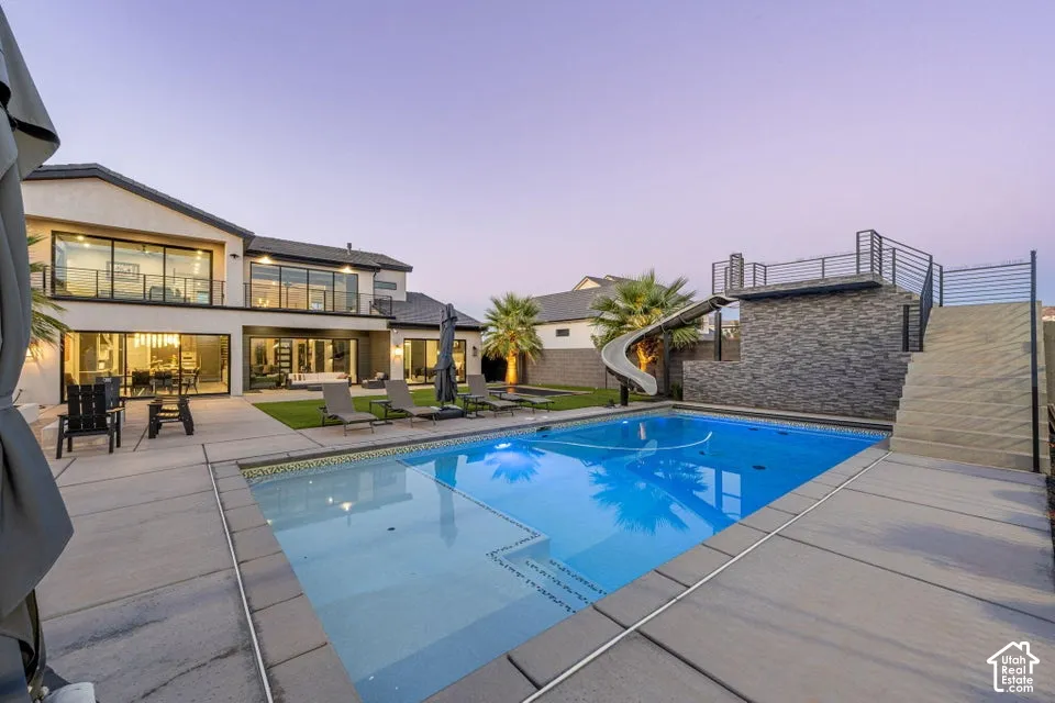 Expansive rear patio featuring a rectangular swimming pool, integrated slide, and a multi-level stone-clad structure