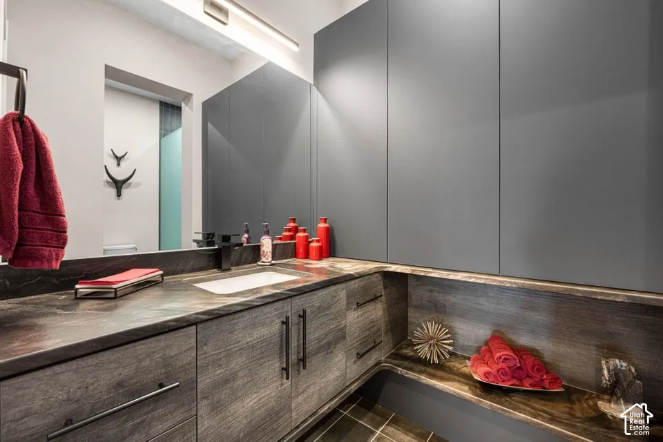Integrated vanity with a rectangular sink, dark stone countertop, modern wall-mounted lighting, and gray flat-panel cabinetry