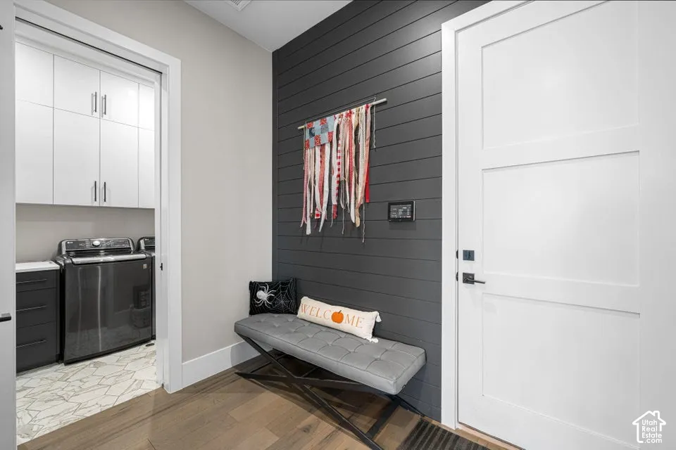 Wood-finish flooring, white paneled door, dark accent wall with horizontal paneling, built-in overhead cabinetry in laundry area, and laundry room with patterned tile flooring