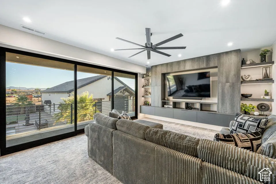 Wide sliding glass doors, built-in media console with integrated shelving, recessed lighting, and a modern ceiling fan