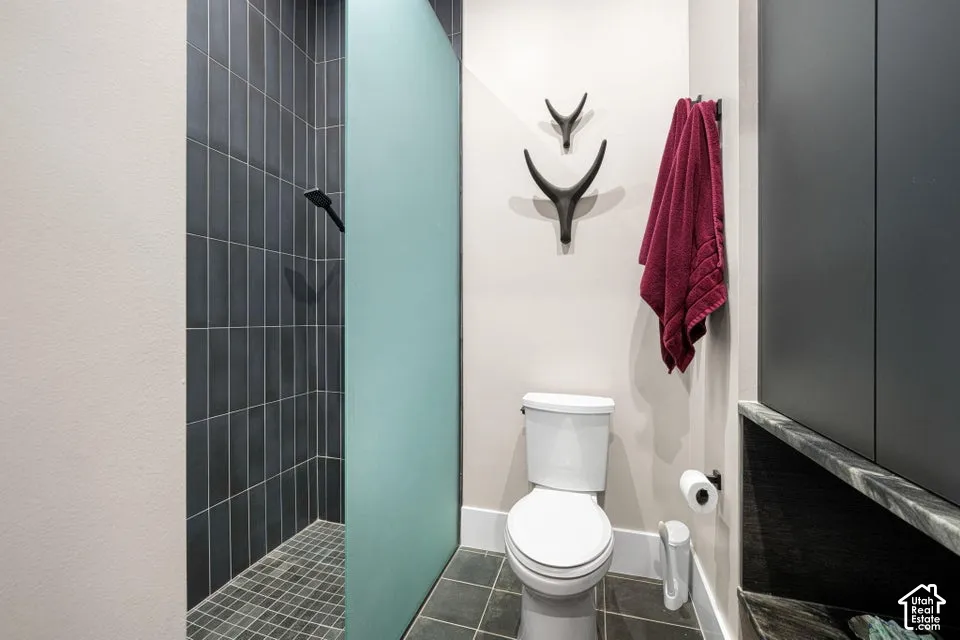 Shower with dark vertical tile surround and mosaic tile flooring, frosted glass shower partition, and built-in cabinetry with stone countertop