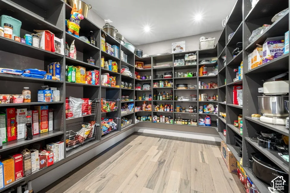 Spacious pantry featuring extensive built-in shelving, wood-finish flooring, and recessed ceiling lighting