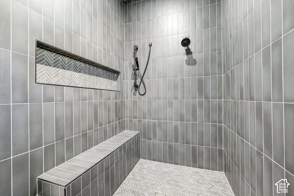 Spa-inspired shower enclosure featuring vertical subway tile walls, a built-in bench seat with mosaic tile detailing, recessed shelving with geometric tile inlay, dual showerheads with handheld sprayer, and brushed black fixtures