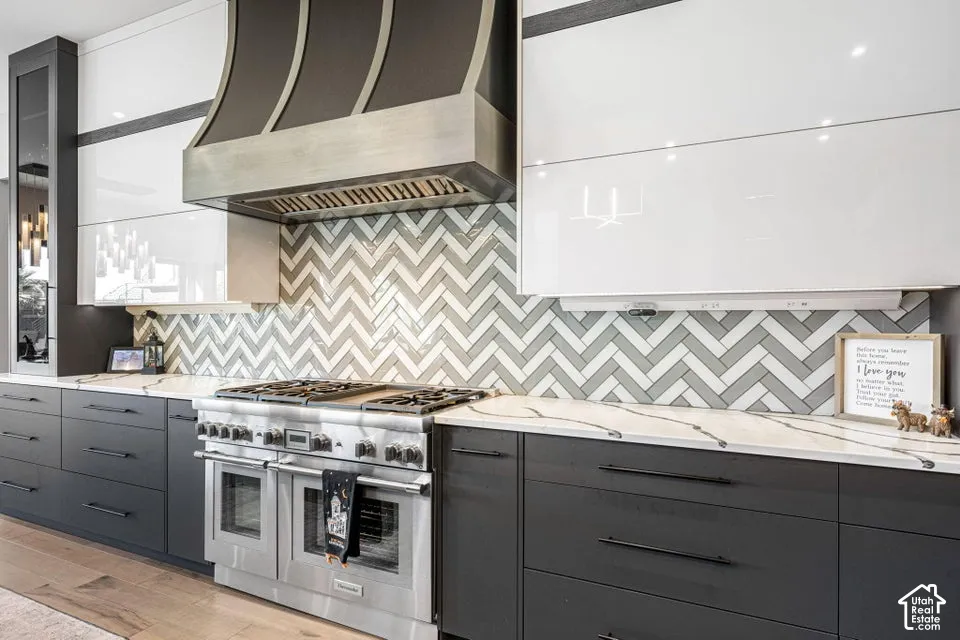 Stainless steel professional-grade range, herringbone tile backsplash, white countertops with dark veining, two-tone cabinetry with dark lower and white upper cabinets, and a prominent stainless steel range hood
