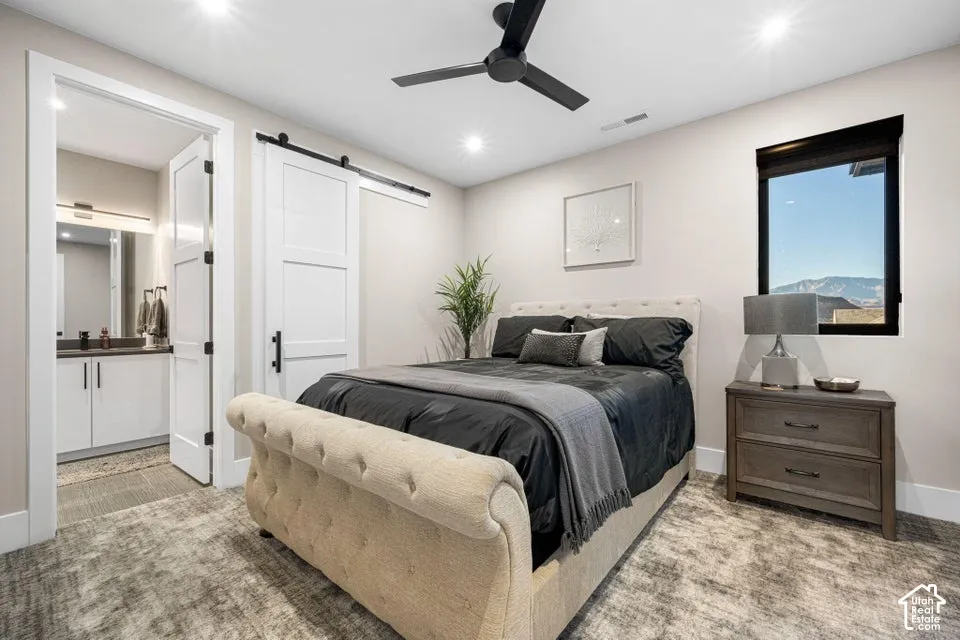 Recessed lighting, ceiling fan, wide window with dark trim, white barn door, and a private bathroom with a vanity