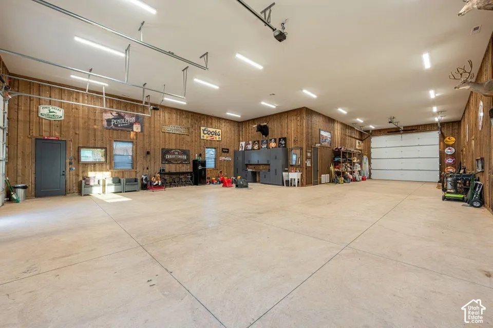 Spacious garage with light-toned concrete flooring, wood-paneled walls, multiple garage doors, and abundant overhead lighting