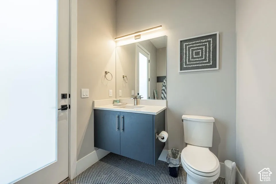 Floating vanity with a white countertop and dark cabinetry, complemented by a square mirror with linear overhead lighting, and hexagonal floor tiling